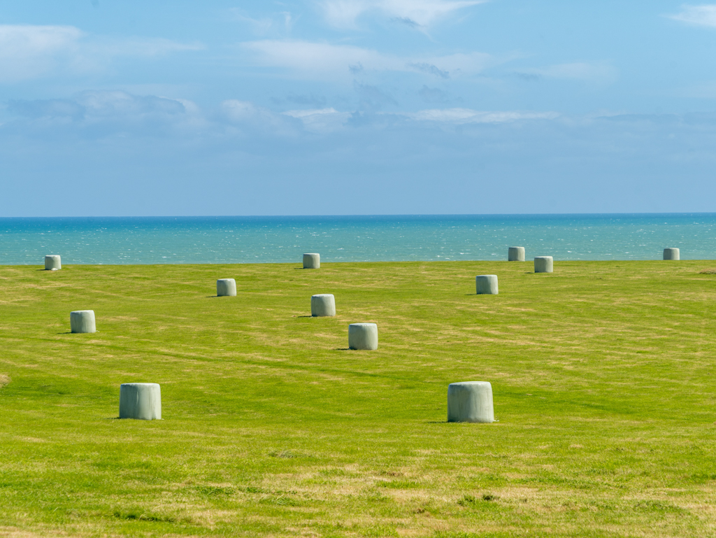 Blaugrünes Stilleben mit umwickelten Heuballen, gemähtem Feld, dem Meer und dem Himmel...