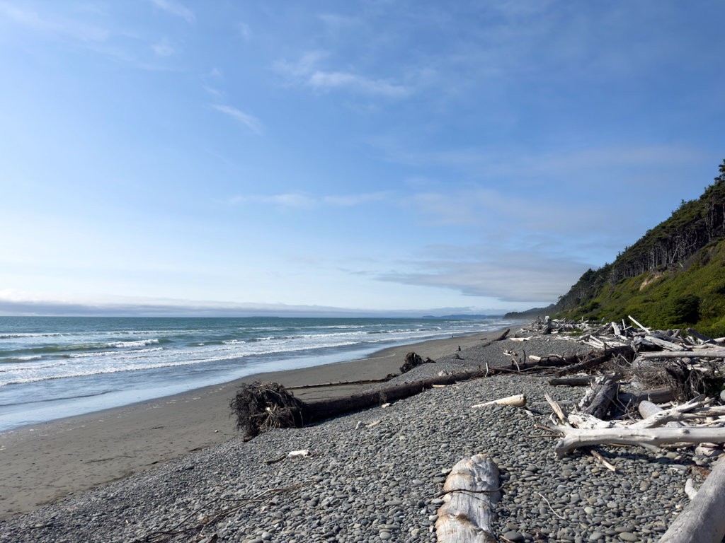 Kalaloch Beach mit viel Treibholz, das die steile Küste vor dem Erodieren schützt und flachen, runden Kieseln und Steinen