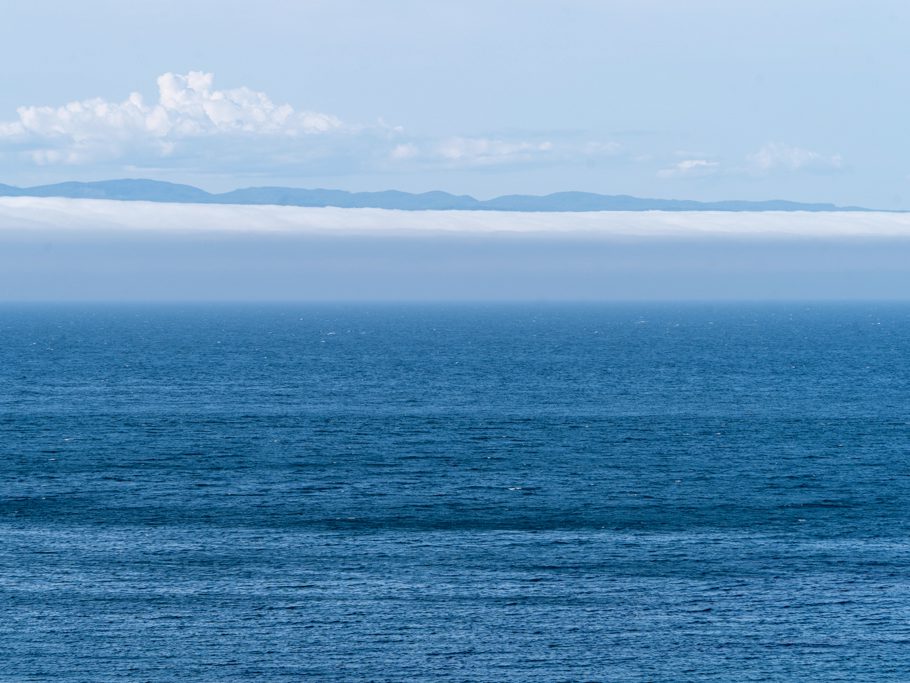 Tief blaues Meer, Nebel- oder Wolkenbänke und im Hintergrund Vancouver Island