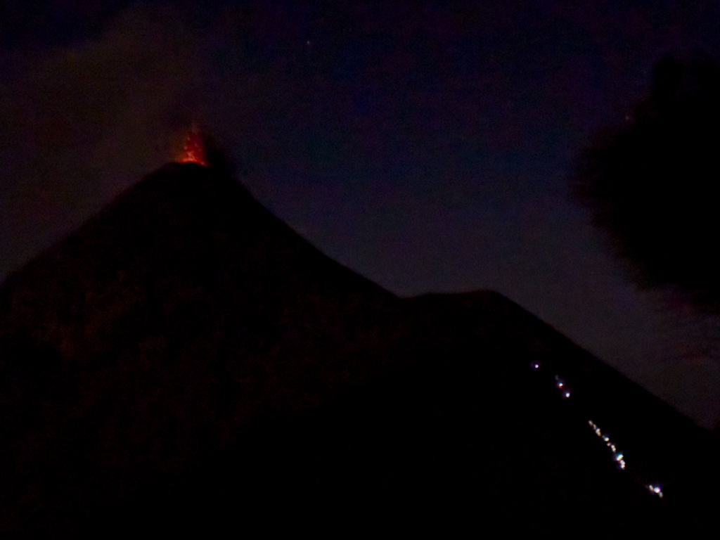 Fuego spuckt Feuer und Rauch in der Nacht. Rechts die Lichterschlange einer Gruppe die auf dem Retourweg sind
