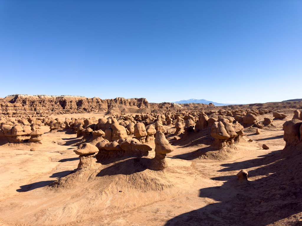 Ein grosses Feld mit vielen kleinen Goblins und einer hohen roten Felswand im Goblin Valley State Park
