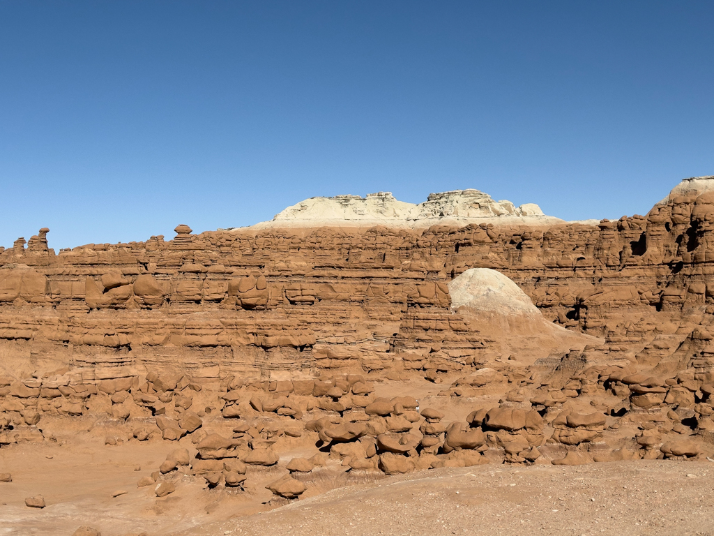 Ein grosses Feld mit vielen kleinen Goblins und einer hohen roten Felswand im Goblin Valley State Park