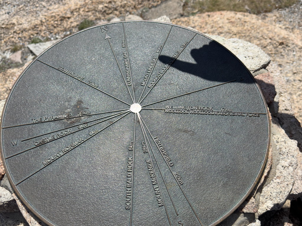 Erklärungsscheibe zu den Himmelsrichtungen und den sichtbaren Bergen umher. Jo zeigt auf Mt. Lindesay in 86 km Entfernung