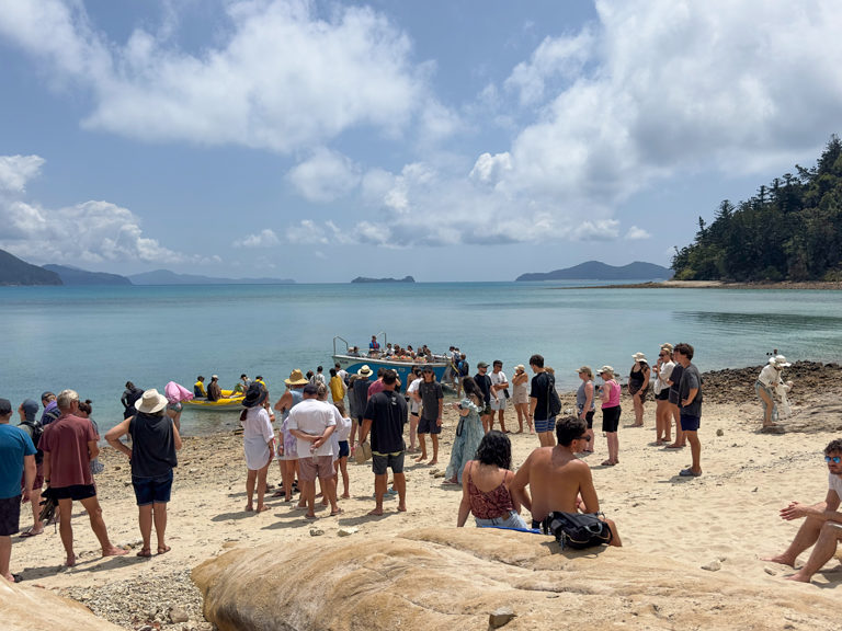 Alle Gäste warten an Strand auf die Dingis die sie auf die Boote verteilen