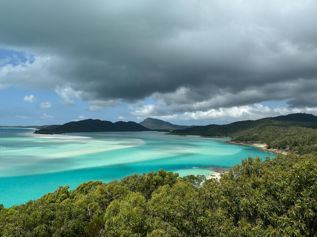 Südseepanorama:wie sanfte Wellen zeichnet sich der weisse Sand unter dem flachen Wasser ab. Weiter leerer Strand mit ein paar wenigen Booten in der Bucht