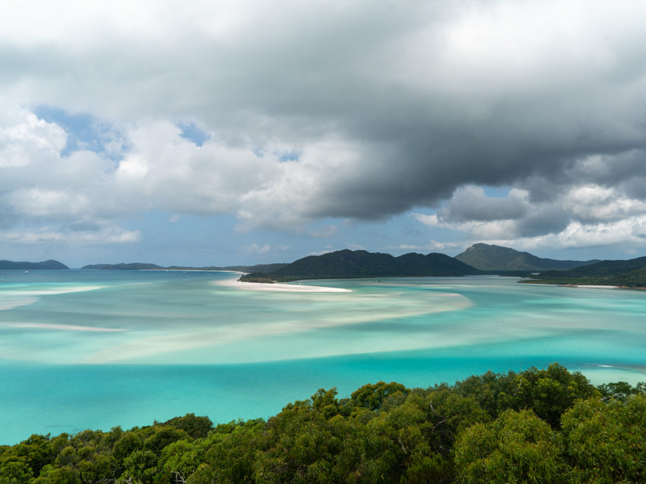 wie sanfte Wellen zeichnet sich der weisse Sand unter dem flachen Wasser ab. Weiter leerer Strand mit ein paar wenigen Booten in der Bucht