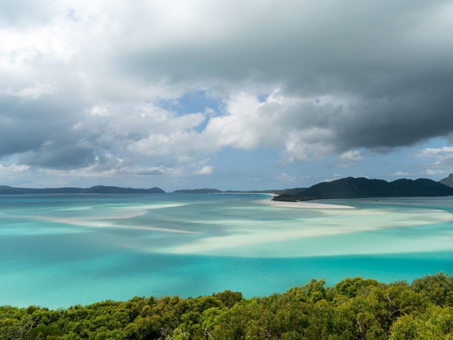Südseepanorama:wie sanfte Wellen zeichnet sich der weisse Sand unter dem flachen Wasser ab. Weiter leerer Strand mit ein paar wenigen Booten in der Bucht
