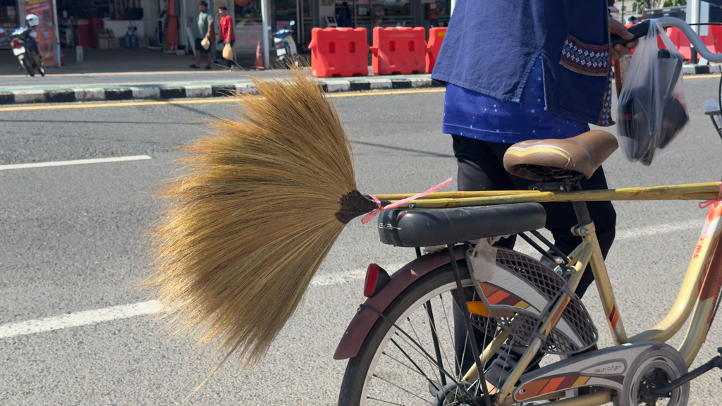 Ein traditionell gefertigter Besen wird auf einem Velo transportiert