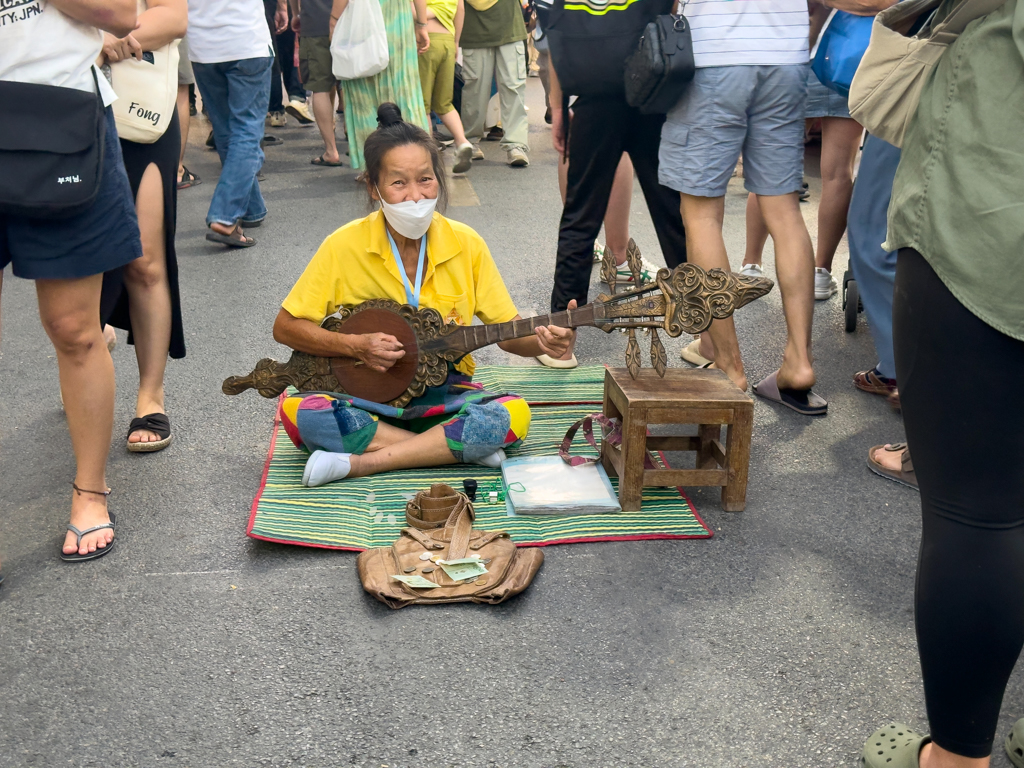 Eine Musikerin spielt ihre Weisen zwischen all den Beinen hockend am Boden