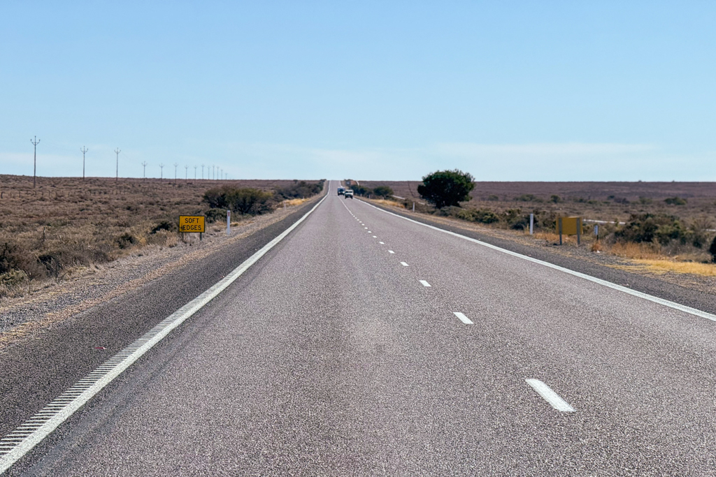 Links neben dem Stuart Hwy ein paar Stromleitungen, sonst nur diese lange gerade Strasse mit ab und zu ein paar Autos, die uns entgegenkommen