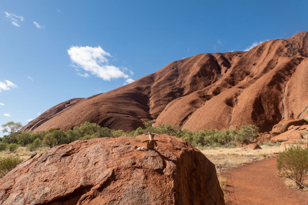Mo posiert auf einen roten Fels vor dem grossen roten Felsen mit Namen Uluru