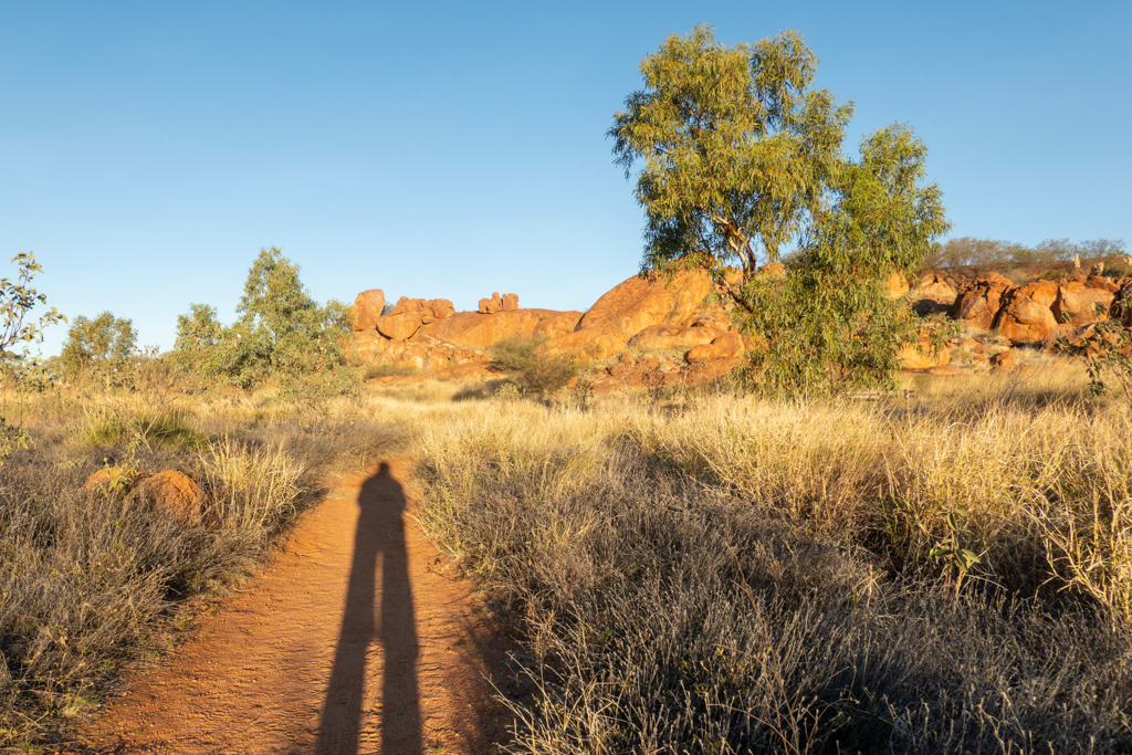 Ma's langer Schatten im untergehenden Sonnenlicht bei den Devils Marbles