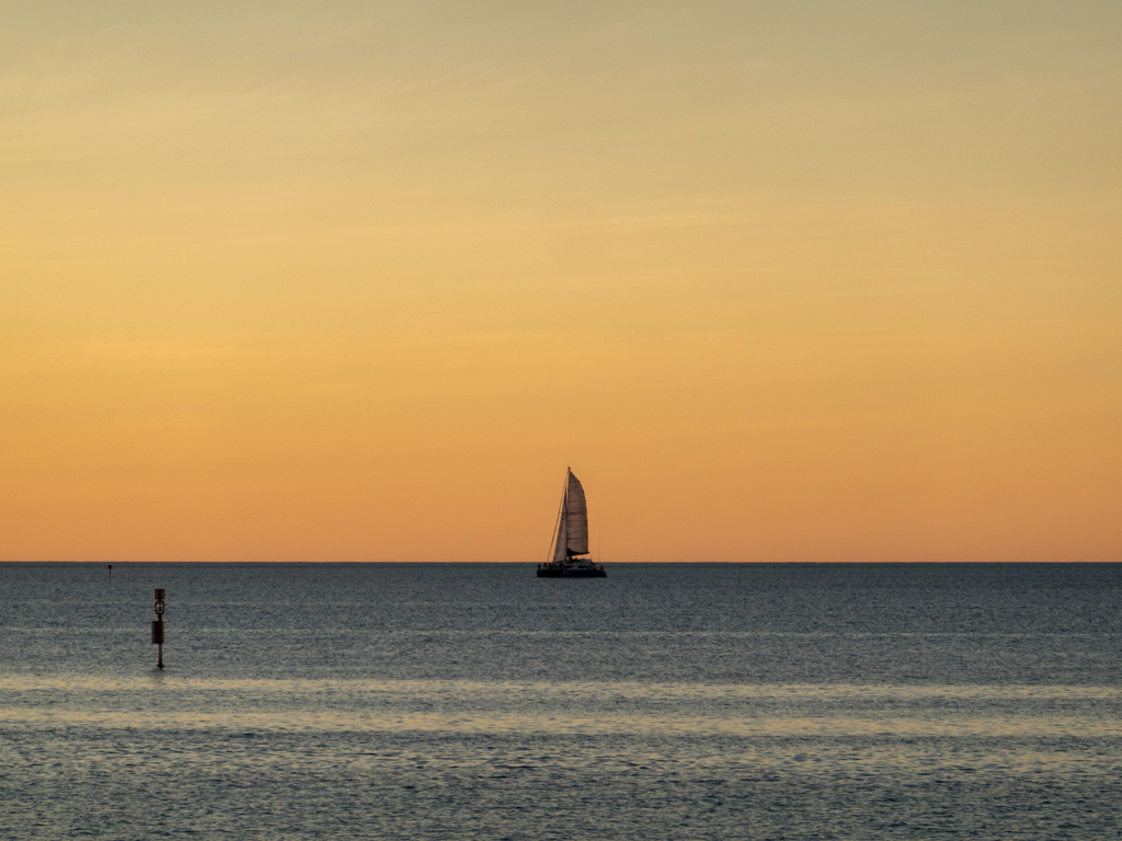 Die Silhouette eines Segelbootes hebt sich gegen den Abendhimmel ab.