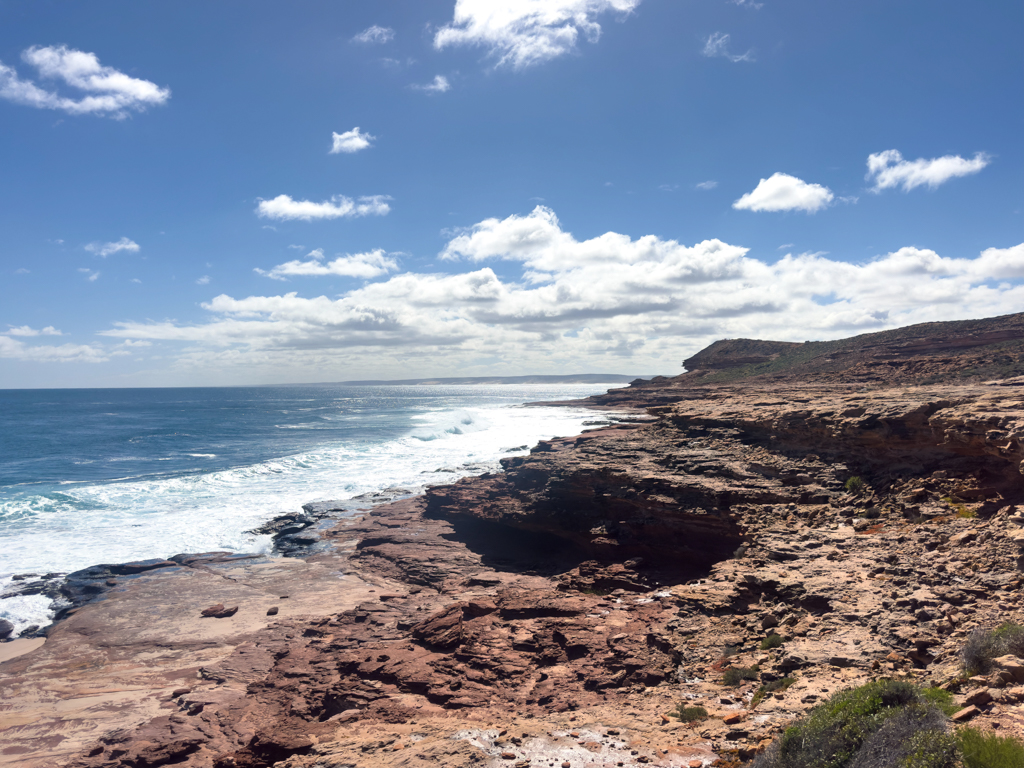 Während unten ewig das Meer an die Küste der Kalbarri Beach brandet ziehen am blauen Himmel weisse Wolken vorbei